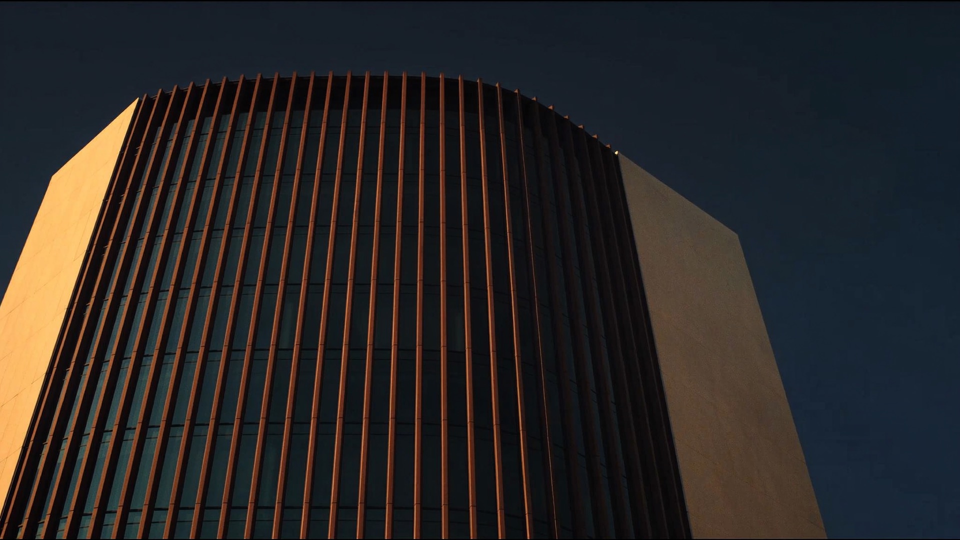 Curved tower facade with bronze fins against an evening sky